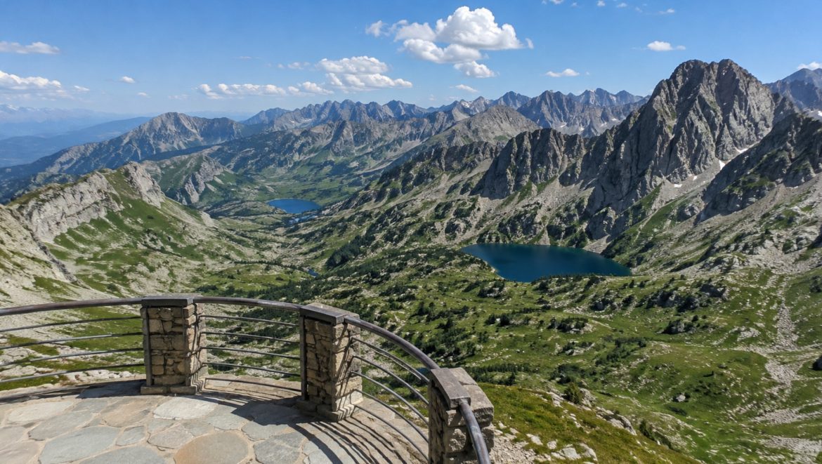 Terrasse d'un belvédère en pierre dominant une vallée des Pyrénées, ses lacs d'altitude turquoise et ses crêtes rocheuses